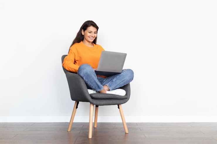 Foto feliz bonita mujer india sentada en un sillón usando una laptop
