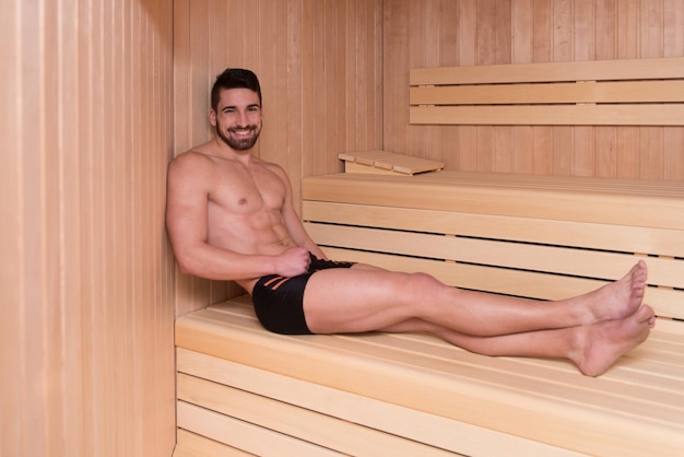 Feliz, bonito e atraente jovem com corpo musculoso relaxante na sauna quente