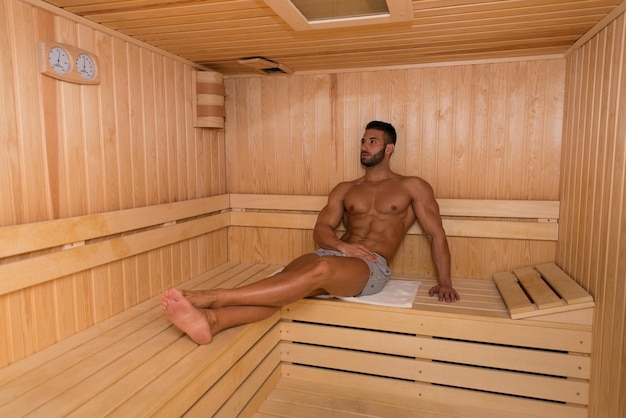 Feliz, bonito e atraente jovem com corpo musculoso relaxante na sauna quente