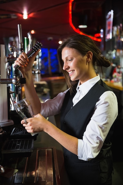 Feliz camarera tirando una pinta de cerveza en un bar