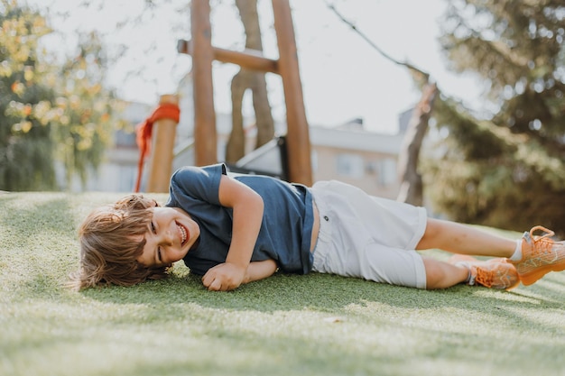 Feliz cansado después de entrenar al niño yace en la hierba verde y descansa, el niño se dedica a los deportes al aire libre