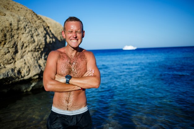 Feliz cara alegria de férias, fica na costa e olha para o mar. shorts masculinos, sol, praia