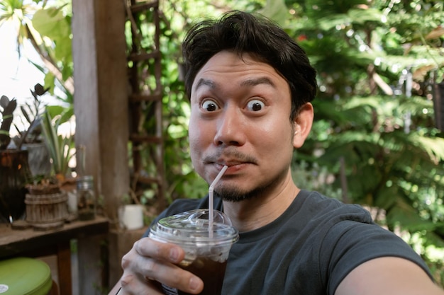 Feliz cara divertida hombre asiático selfie a sí mismo bebiendo café helado fresco en el café