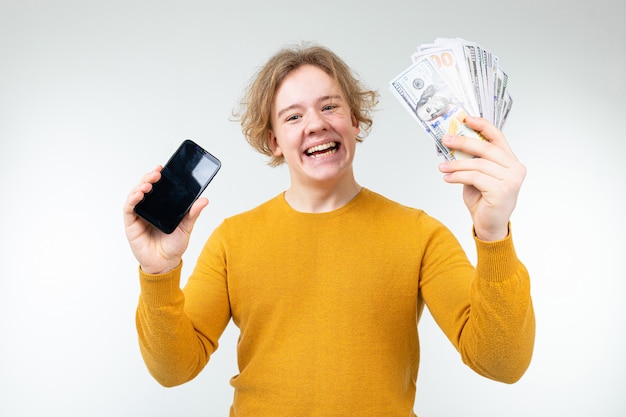 Feliz cara loiro mantém seu salário e smartphone com uma maquete em um branco