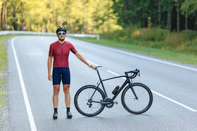 Feliz cara musculoso com capacete preto e óculos espelhados relaxando no rad após o passeio matinal