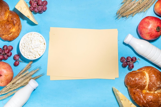 Feliz cartão de felicitações de Shavuot com comida Símbolos do feriado judaico de Shavuot romã uvas maçã doce chalá pão espigas de trigo leite queijo cottage requeijão em fundo azul claro