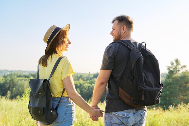 Feliz casal adulto com mochilas de mãos dadas vista traseira