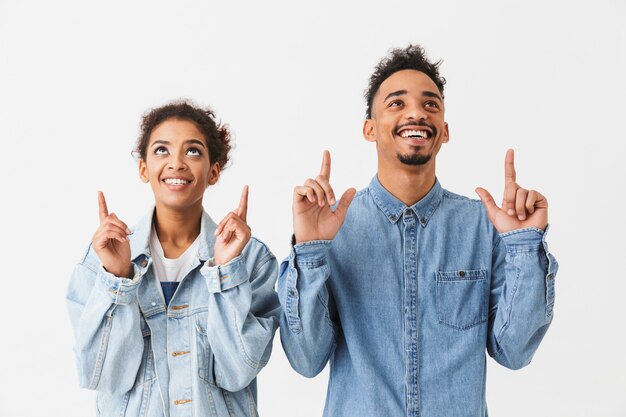 Feliz casal Africano apontando com o dedo indicador e olhando por cima da parede cinza