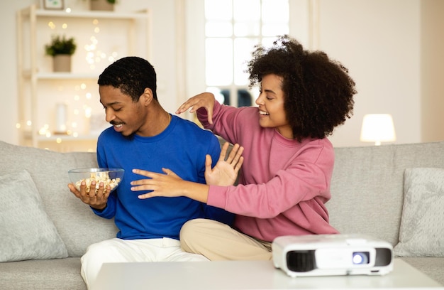 Feliz casal africano assistindo filme via projetor brincando em casa