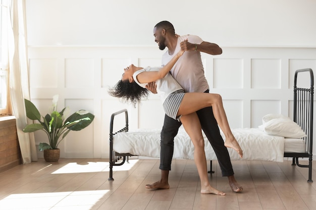 Foto feliz casal afro-americano de pijama dançando balançando no quarto animado movendo-se juntos alegremente sorridentes marido e esposa dançarinos birraciais se divertem celebrando em casa o conceito de objetivo de relacionamentos