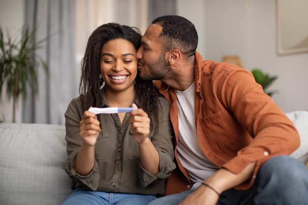 Feliz casal afro-americano segurando teste de gravidez positivo em casa