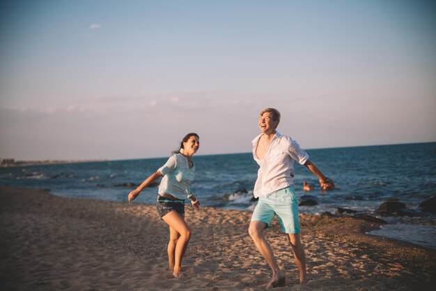 Feliz casal apaixonado contra o mar anda na praia contra o céu azul e se diverte no dia de verão União ama a família