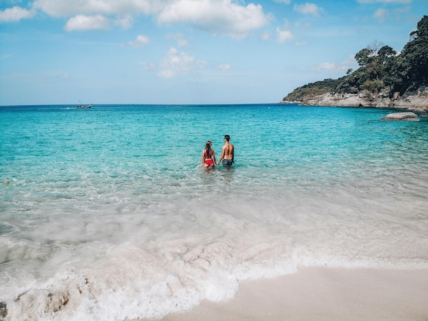 Feliz casal apaixonado dançando na água azul perto da praia; conceito de lua de mel.