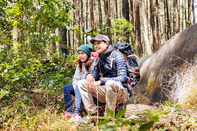 Feliz casal asiático caminhantes sentar em um tronco de árvore enquanto descansava