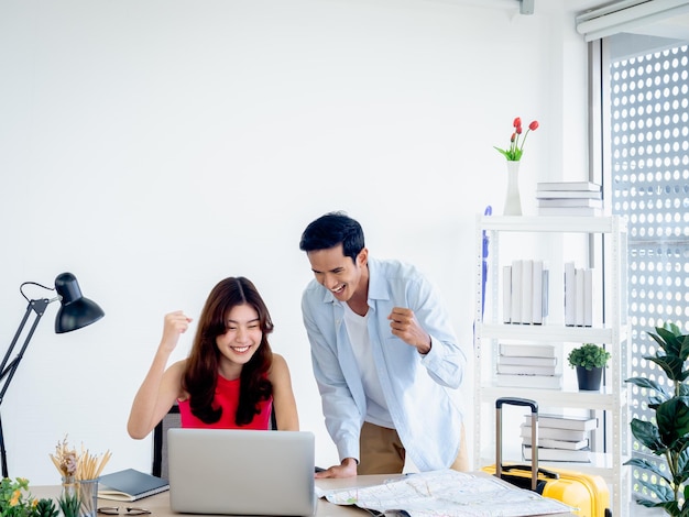 Feliz casal asiático jovem e homem usando computador portátil junto com o sentimento de sucesso ao levantar o punho e sorrir após a reserva para a viagem de verão pronta para viajar conceito de férias felizes