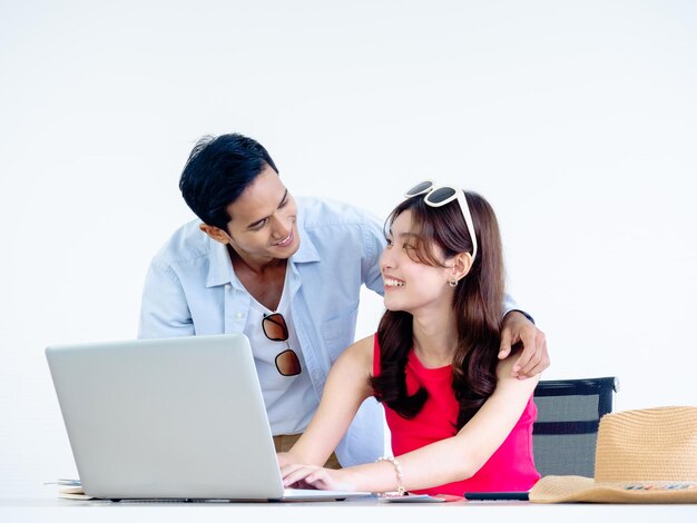 Feliz casal asiático jovem e homem usando computador portátil na mesa juntos para reserva de voo quarto de hotel e informações de viagem no escritório pronto para viajar conceito de férias de verão de férias felizes