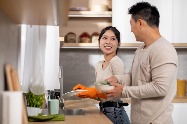 Feliz casal asiático lavando pratos juntos em casa