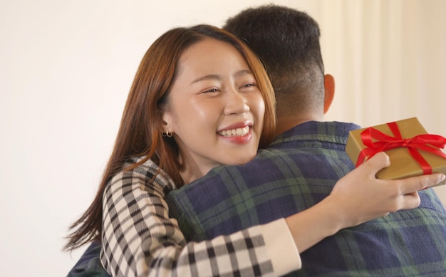 Feliz casal asiático se abraçando apaixonado em casa comemorando dando uma caixa de presente no dia do aniversário