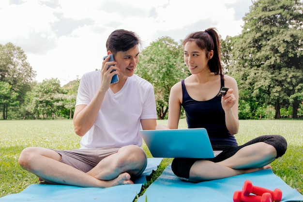 Feliz casal asiático usa laptop para comprar equipamentos de ginástica on-line com cartão de crédito