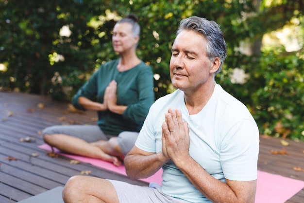 Feliz casal caucasiano sênior praticando ioga, meditando no jardim ensolarado. estilo de vida saudável de aposentadoria, passando o tempo em casa.