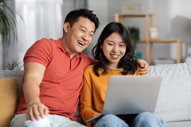 Feliz casal chinês usando laptop juntos interior de casa