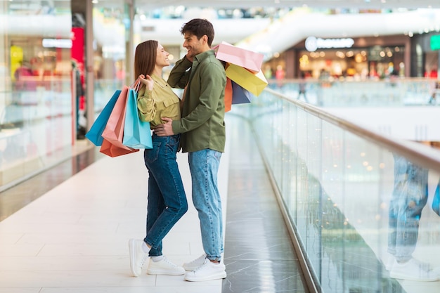 Feliz casal de compradores fazendo compras juntos em pé abraçando no shopping