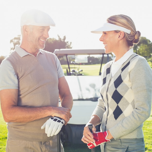 Feliz casal de golfe conversando com buggy de golfe por trás