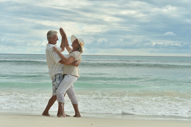 Feliz casal de idosos dançando na praia tropical