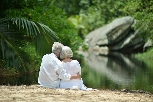 Feliz casal de idosos sentado na praia tropical