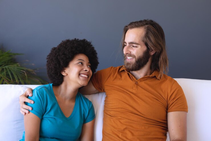 Foto feliz casal diversificado sentado no sofá, abraçando e sorrindo