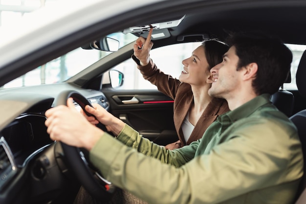 Foto feliz casal do milênio testando carro novo na concessionária de automóveis