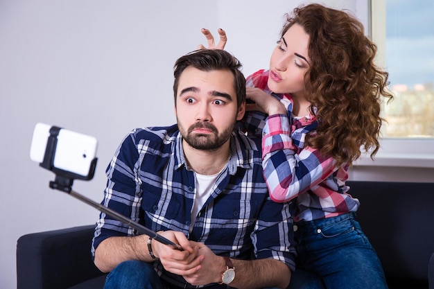 Feliz casal engraçado tirando foto com o celular no pau de selfie em casa