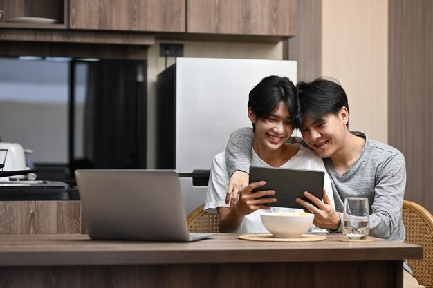 Feliz casal gay abraçando e navegando na internet com tablet digital juntos na mesa da cozinha relacionamentos de orgulho LGBT e conceito de igualdade