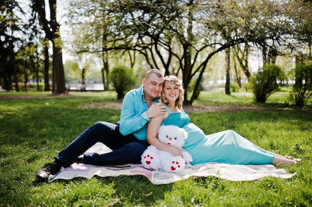 Feliz casal grávido abraçando e sentado na natureza da primavera de fundo xadrez