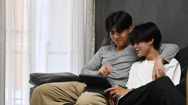 Feliz casal homossexual abraçando e usando tablet digital juntos no sofá LGBT e conceito de amor