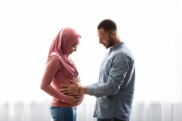 Feliz casal islâmico grávida negra juntos perto da janela em casa