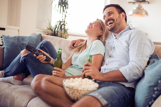 Feliz casal jovem deitado no sofá em casa assistindo TV