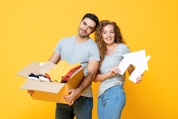 Feliz casal jovem e alegre carregando coisas em fundo de estúdio isolado amarelo, mudança de casa e conceito de realocação