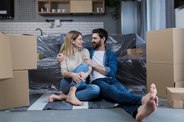 Feliz casal jovem homem e mulher em casa sentados no sofá no novo apartamento alugado perto de caixas de papelão