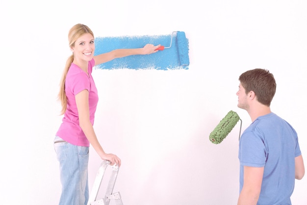 Foto feliz casal jovem pinta na parede branca de cor verde e azul de sua nova casa