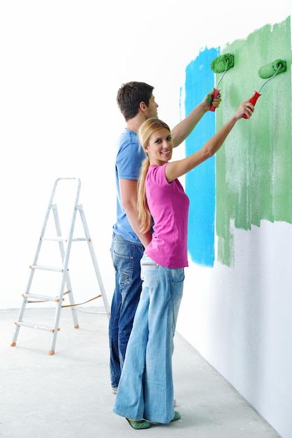 Feliz casal jovem pinta na parede branca de cor verde e azul de sua nova casa