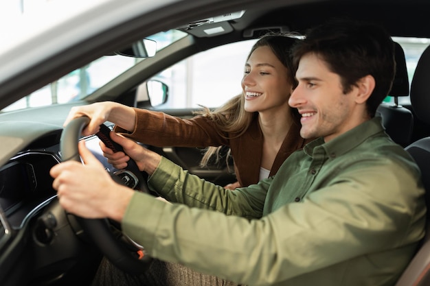 Feliz casal jovem testando carro novo na concessionária moderna