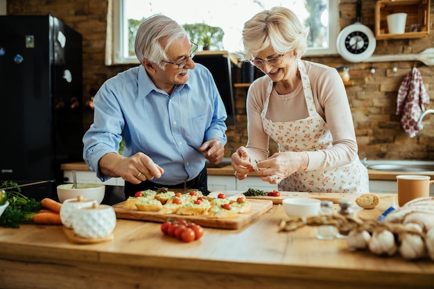 Feliz casal maduro conversando e se divertindo enquanto faz bruschetta juntos na cozinha