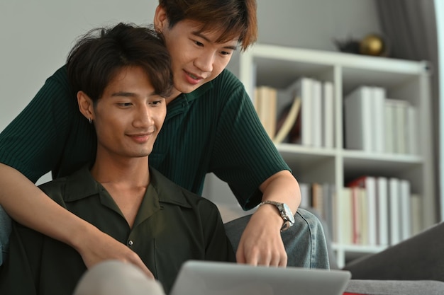 Feliz casal masculino do mesmo sexo abraçando e usando laptop na sala de estar Amor LGBT e conceito de relacionamento de estilo de vida