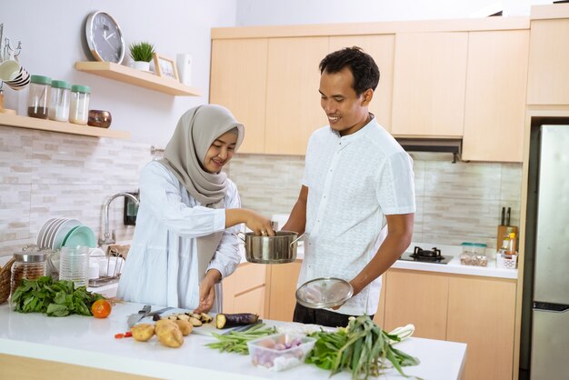 Feliz casal muçulmano cozinhando juntos na cozinha. homem e mulher se preparando para o jantar