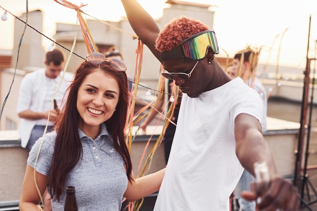 Feliz casal multirracial Grupo de jovens em roupas casuais fazem uma festa no telhado juntos durante o dia