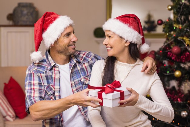 Feliz casal no chapéu de Santa segurando presente