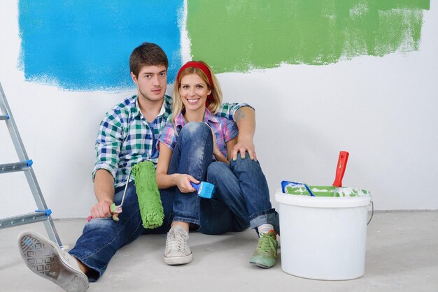 Feliz casal relaxa depois de pintar a parede branca na cor verde e azul em sua nova casa