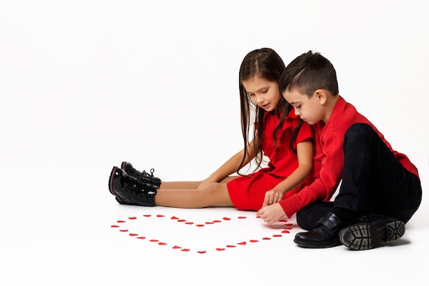 Feliz casal romântico menina e menino fazem um grande coração com pequenos corações de papel no chão