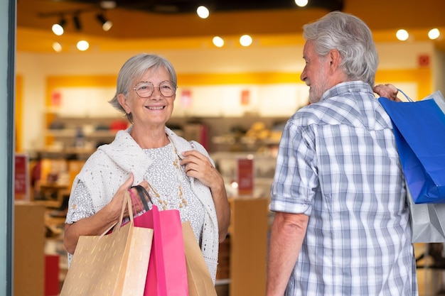 Feliz casal sênior carregando sacolas de compras aproveitando o conceito de cliente de vendas de consumismo de compras